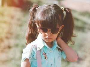 Petite fille stylée avec des lunettes de soleil de marque et une chemise bleue.