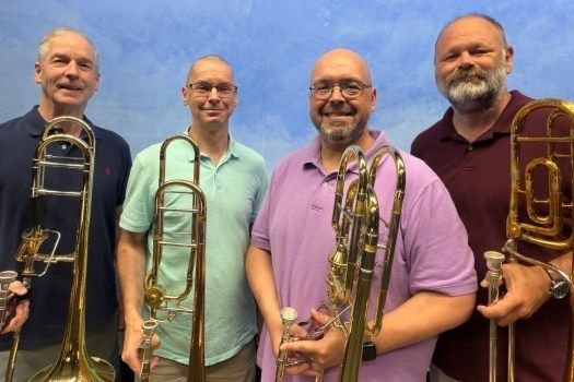 Quatre musiciens posent avec leurs trombones dans un ensemble de cuivres